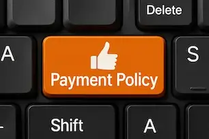 Keyboard with orange "Payment Policy" key and thumbs-up icon next to black keys like Shift and Delete.