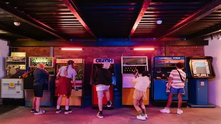 Players standing at classic arcade cabinets in a retro video game arcade.
